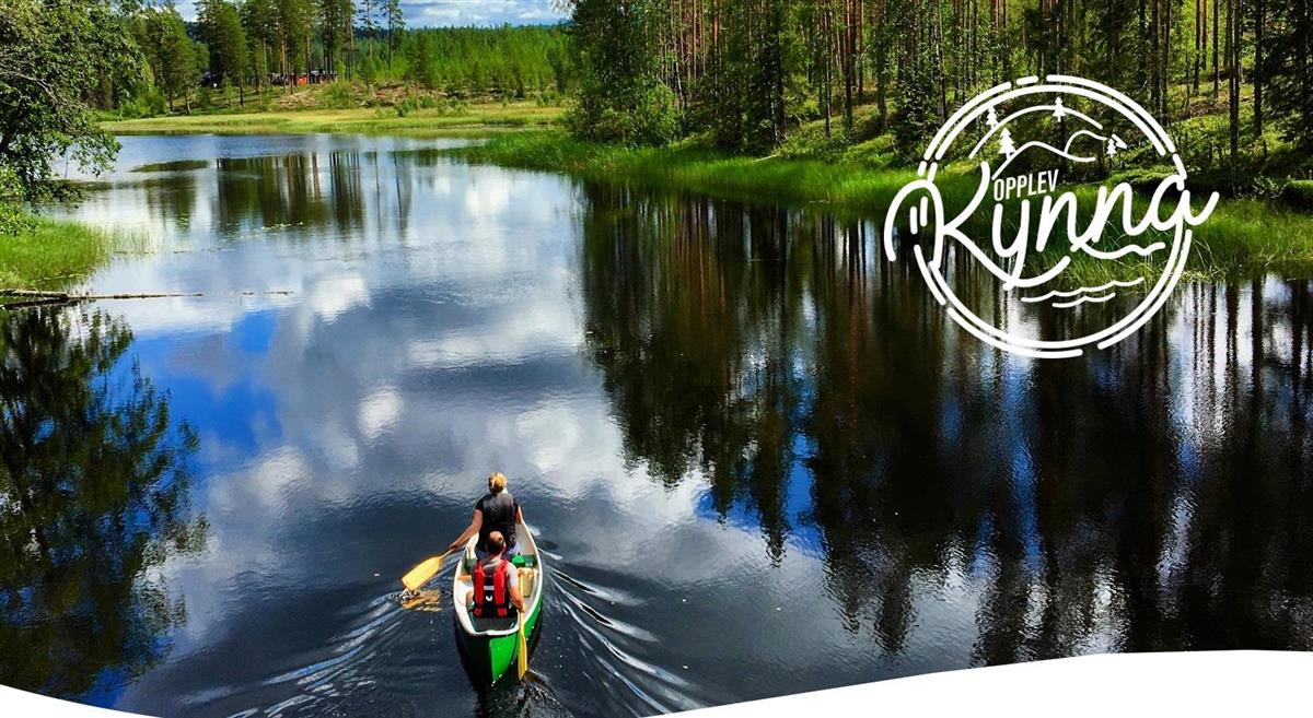 Kano på vann. Skogslandskap i bakgrunnen. - Klikk for stort bilde