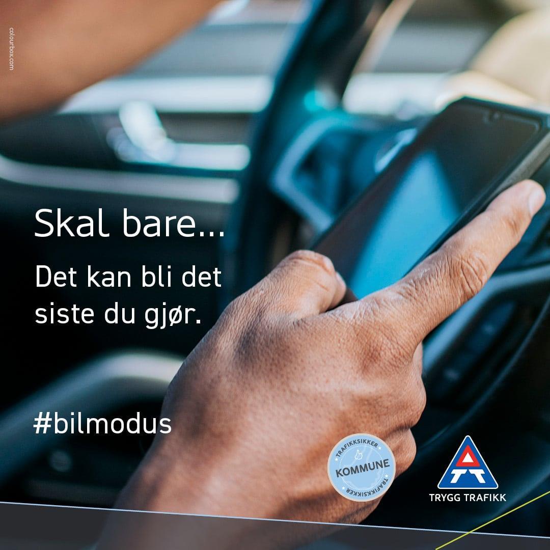 Tekstplakat med bilde av hånd som holder i en mobiltelefon mens personen sitter bak rattet på en bil. - Klikk for stort bilde