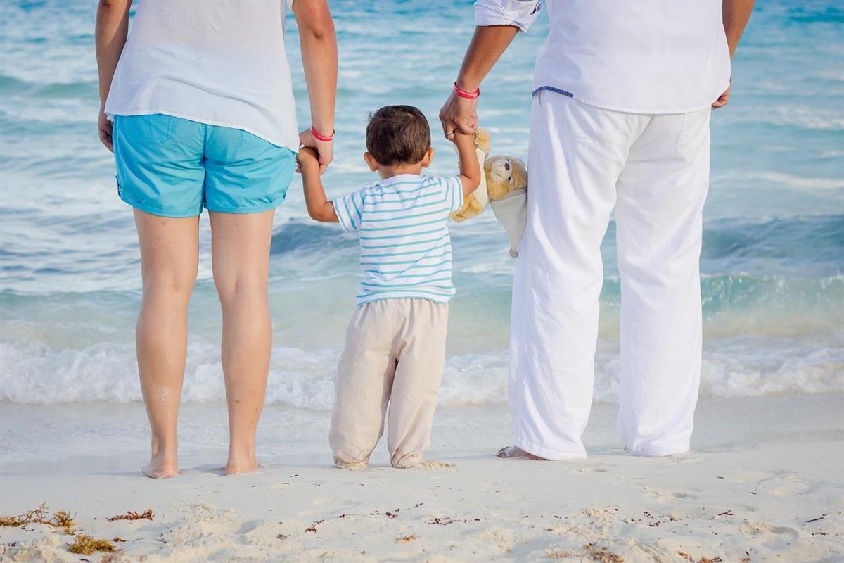 To voksne personer som holder et barn i hånden på en strand. - Klikk for stort bilde
